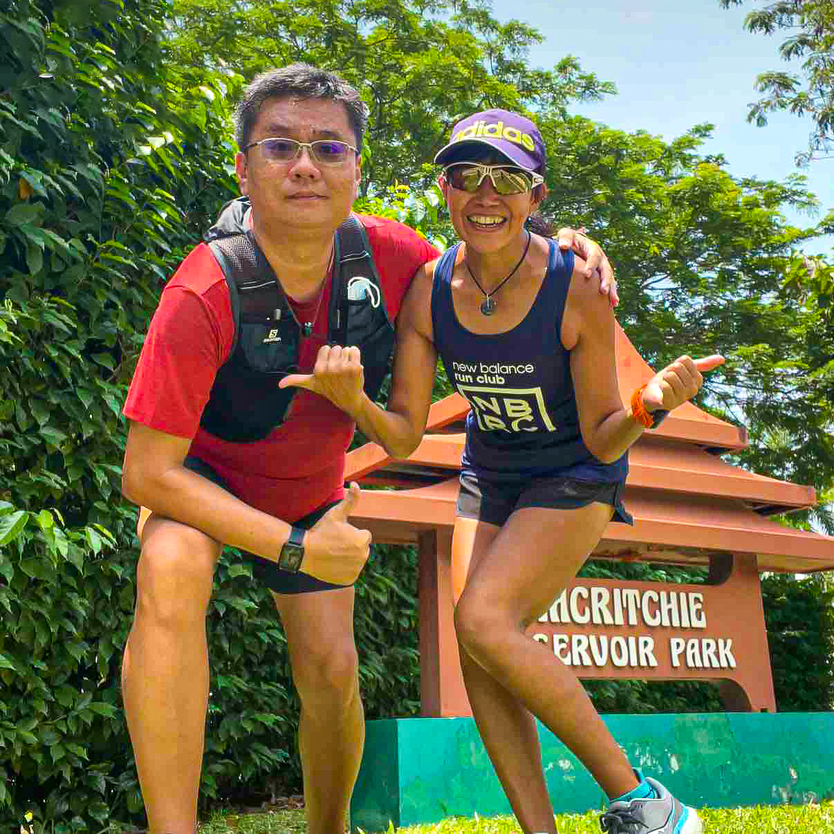 This image features a husband and wife posing in front of Macritchie Reservoir's signage before they embark on a hike. They are both showing the thumbs-up sign.